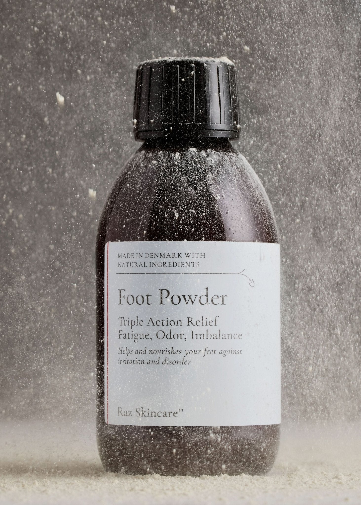 Foot Powder 75g - Raz Skincare - Raz Skincare Foot Powder i brun flaske med sort låg, dækket af dryssende pulverpartikler