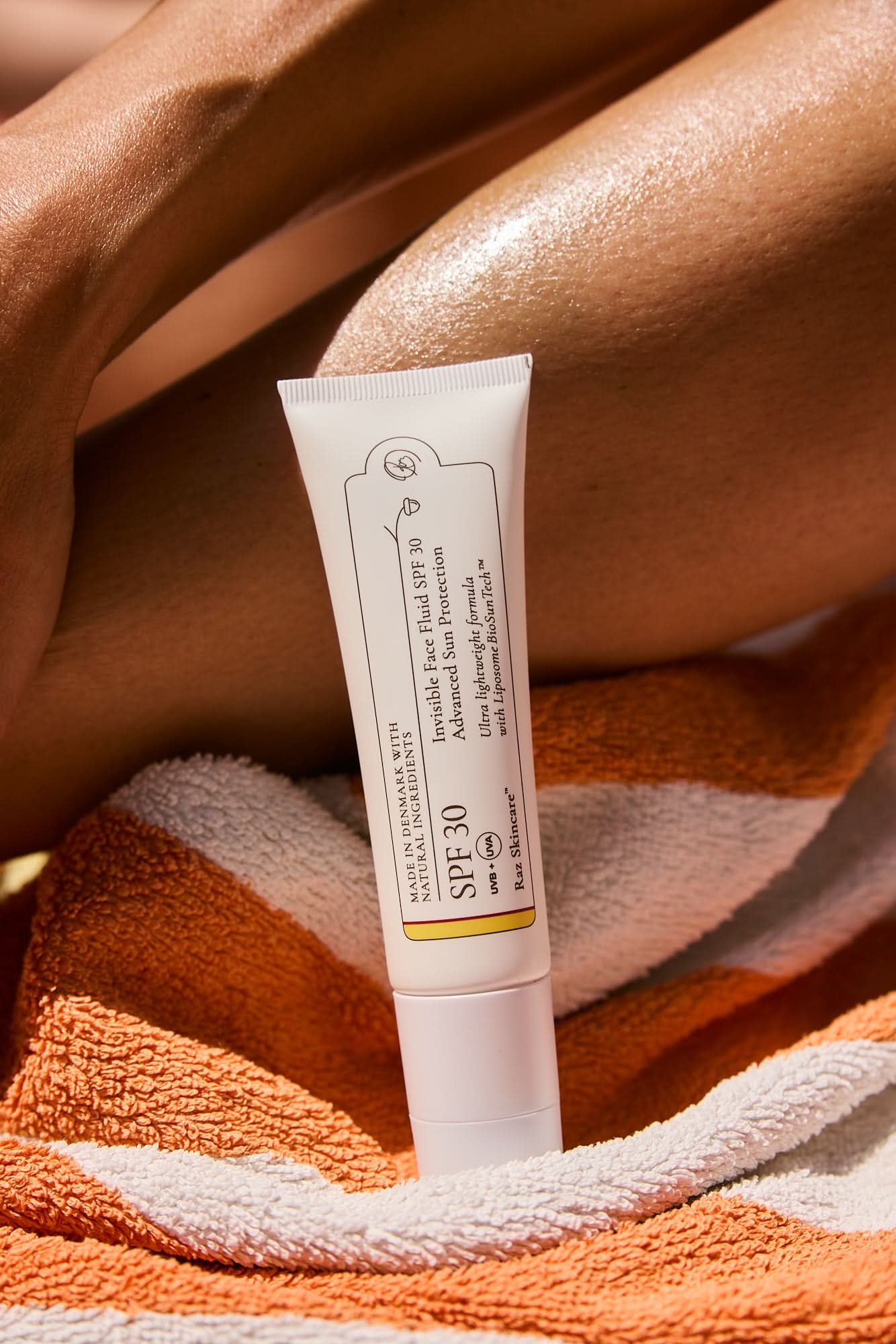 SPF30 Invisible Face Fluid Solcreme 50ml standing on a towel in the sand with a leg in the background